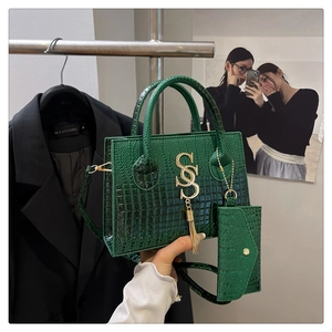 Detail view of dark green croc-embossed handbag with gold hardware and mini pouch charm
