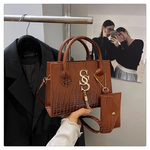 Detail view of brown crocodile texture handbag with gold logo and mini coin purse charm