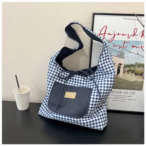 Detail of blue plaid tote bag featuring a denim front pocket and leather fashion label