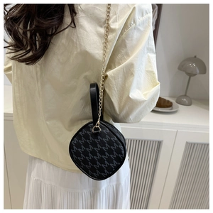 Détail d'un mini sac rond noir avec motif M gris et bandoulière en chaîne dorée