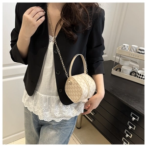 Détail du sac cylindrique crème avec motif M et bandoulière en chaîne dorée