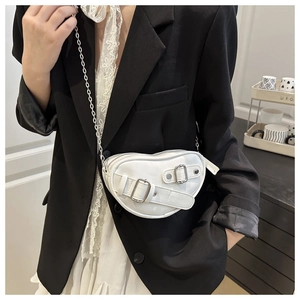 Close-up of white heart-shaped shoulder bag with silver buckle straps and chain