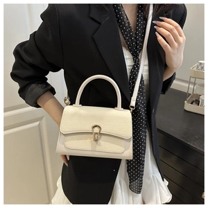 Detail of a creamy white crossbody bag with a shield-shaped metal buckle and woven texture