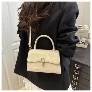 Detail of cream shoulder bag featuring lizard texture flap and golden horseshoe buckle