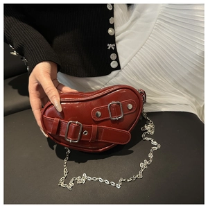 Detail of wine red heart-shaped chain bag with shiny finish and silver buckle straps