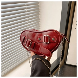 Detail of red heart-shaped handbag featuring textured leather and metal buckle straps