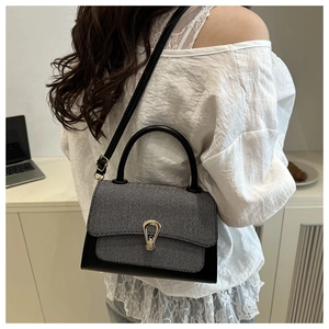Detail of the gray textured fabric and black leather contrast with a gold horseshoe clasp