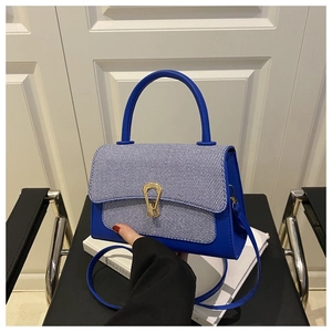 Detail of blue leather bag with striped fabric flap and golden horseshoe clasp