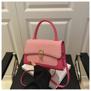Detail of rose pink litchi texture handbag featuring gold horseshoe clasp and woven flap