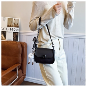Detail of black matte leather crossbody bag with striped ribbon and plush charm