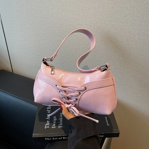 Pink glossy baguette bag with corset lacing and bow detail shown in hand