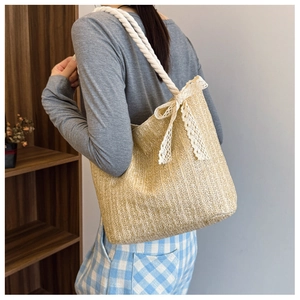 Detail of straw tote bag with lace bow and thick cotton rope handle on female shoulder