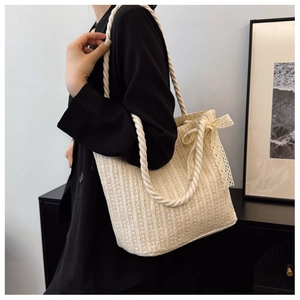 Detail of beige straw tote bag with rope handles and lace bow decoration in side view