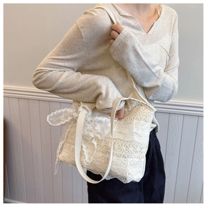Dettaglio borsa a spalla in pizzo beige con motivi floreali e fiocco decorativo