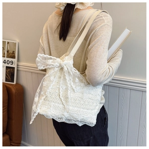 Dettaglio della borsa tote in pizzo bianco con fiocco indossata da una modella in casa