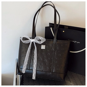 Détail du sac cabas en cuir noir avec motifs gaufrés d'animaux et un nœud en dentelle