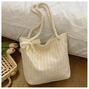 Detail of beige straw shoulder bag with thick cotton rope handles and lace bow decoration