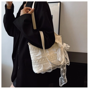 Detail of cream lace tote bag with tiered ruffles and soft bow on black blazer
