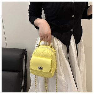 Detail of yellow quilted mini backpack showing silver twist lock and chain strap on a model