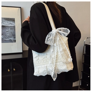Detailed view of white lace tote bag with large ribbon bow on model wearing black blazer