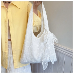 Detailed view of white floral lace embroidery and ribbon bow on a canvas tote bag