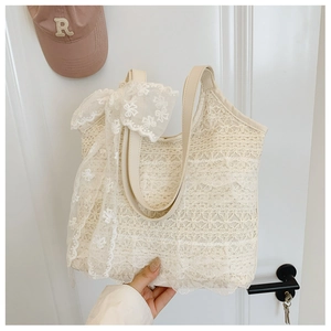 Detail of off-white lace tote bag featuring hollow floral patterns and large lace bow