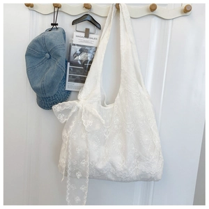 Close-up of white floral lace tote bag with a large decorative bow on a wooden hook