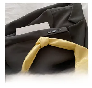 Detail of light yellow glossy handbag featuring a modern knotted handle design on fabric