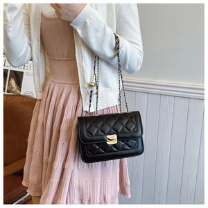 Detail of black quilted chain bag with gold hardware worn by a model in a warm setting