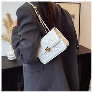 Detailed view of a white quilted crossbody bag with gold chain strap on a grey blazer