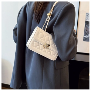 Sac à rabat rectangulaire blanc matelassé avec chaîne dorée sur un blazer sombre