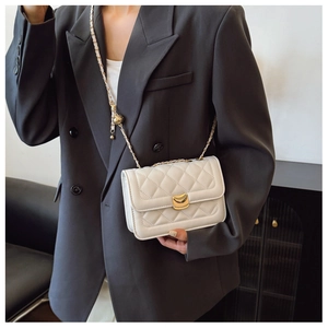 White quilted crossbody bag with gold chain strap worn over a classic black blazer jacket