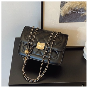 Detail of black quilted leather shoulder bag with gold chain strap and metal lock closure