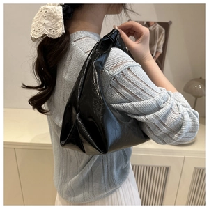Side view of a glossy black underarm bag showing draped texture and metallic shine