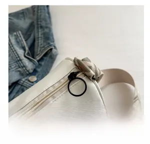Detail of smooth metal ring zipper and colorful geometric woven shoulder strap on white bag
