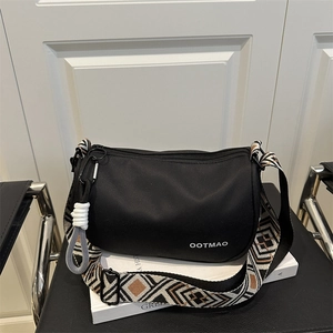 Minimalist black boston bag with geometric woven wide shoulder strap on a modern chair