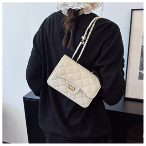 Detail of quilted crossbody bag with gold chain strap worn over a black sweater