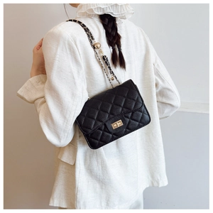 Détail du sac bandoulière matelassé noir avec chaîne dorée porté par un mannequin