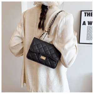 Détail d'un sac bandoulière noir matelassé avec chaîne dorée et breloque boule dorée
