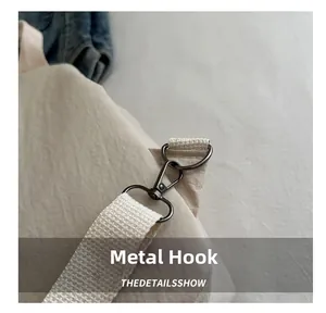 Close-up of dark grey metal spring hook attached to a beige woven crossbody shoulder strap
