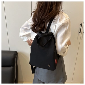Detail shot of black minimalist backpack featuring adjustable straps and iconic red side tag
