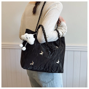 Detail of black tote bag with butterfly metal charms and woven handle with plush charm