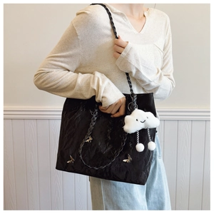 Detail of black pleated shoulder bag featuring metal butterfly and cloud charm accessory