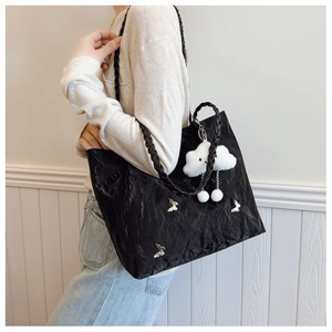 Detail of black pleated tote bag with silver butterfly charm and plush cloud pendant