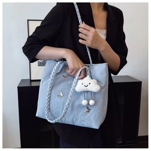 Light blue pleated tote bag with woven strap and gold butterfly charms on black suit