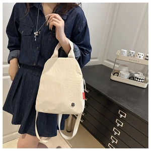 Detail of minimalist beige canvas backpack featuring red fashion label and metallic badge
