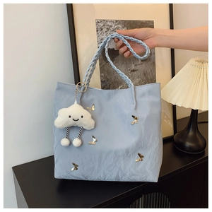 Detail of light blue pleated tote bag featuring golden butterfly charms and braided handles