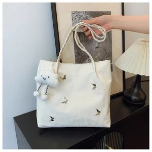 Detail of off-white tote bag with silver butterfly charms and woven handle design
