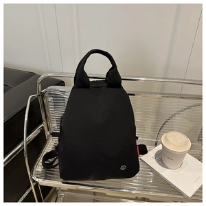 Détail du sac à dos en toile noire montrant l'étiquette rouge et la poignée de transport