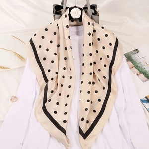 Gros plan d'un foulard en soie beige à pois drapé sur un haut blanc sur un cintre